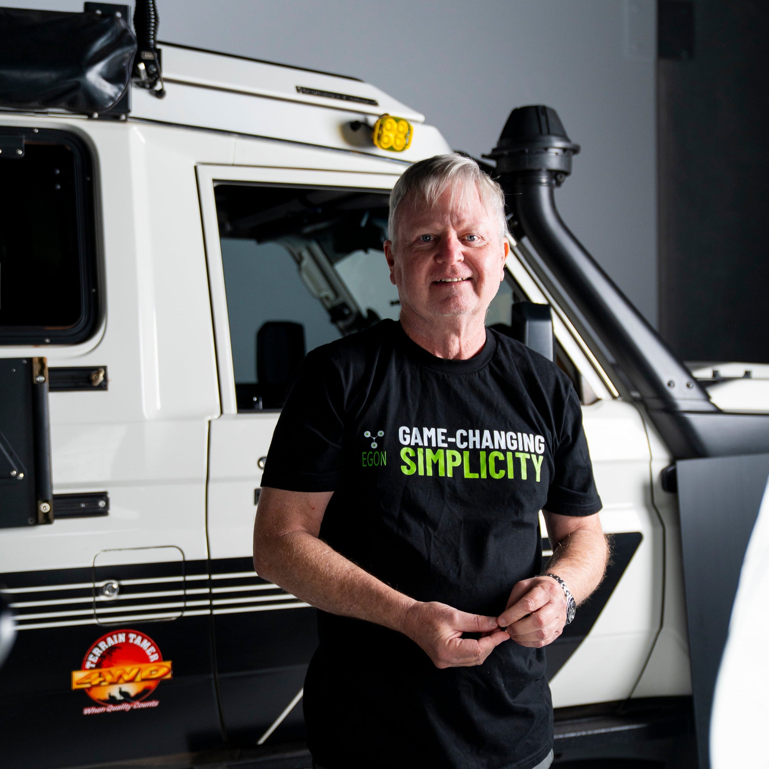 Man standing in front of a vehicle wearing a black t-shirt with text.