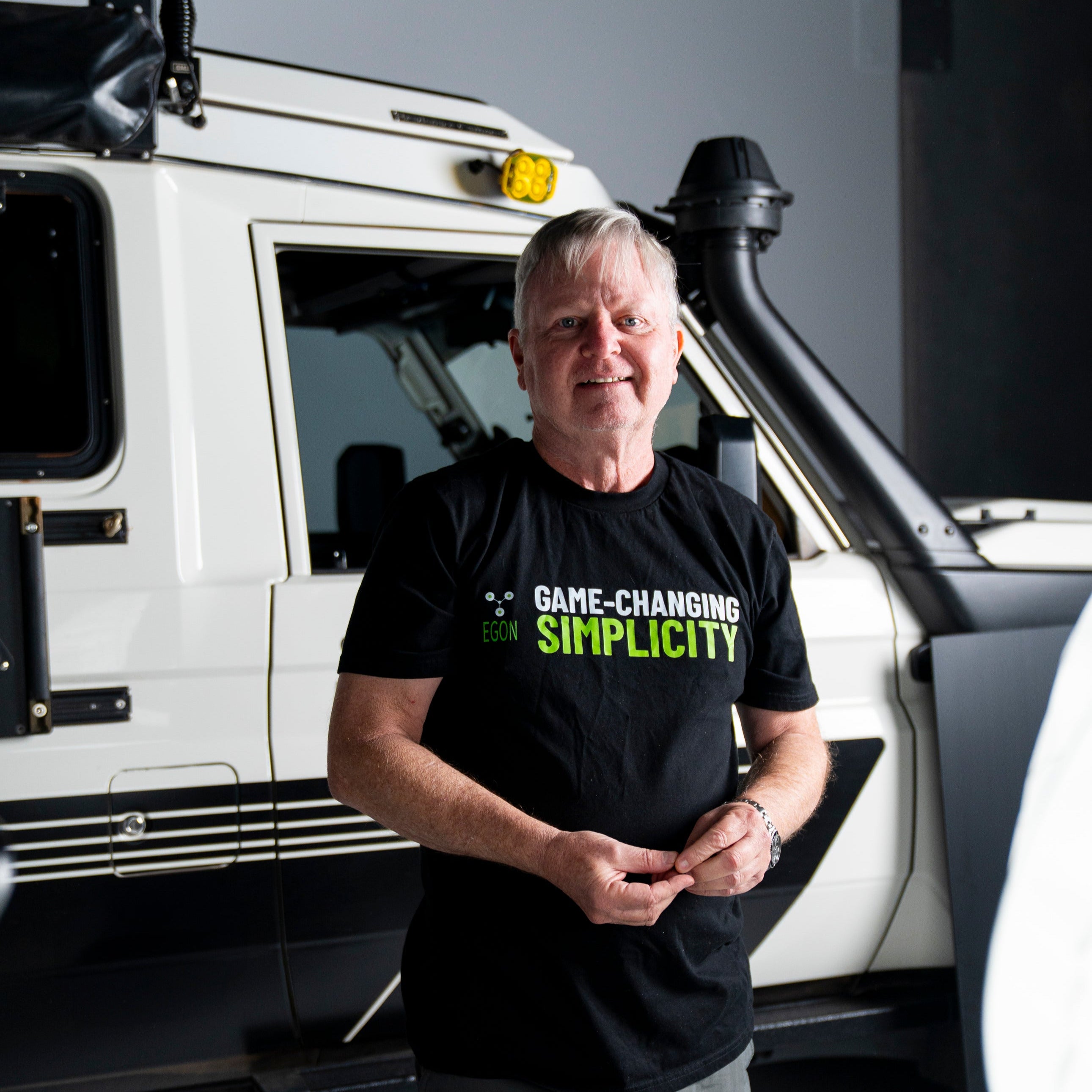 Man standing in front of a white vehicle with 'Game-Changing Simplicity' text on his shirt.