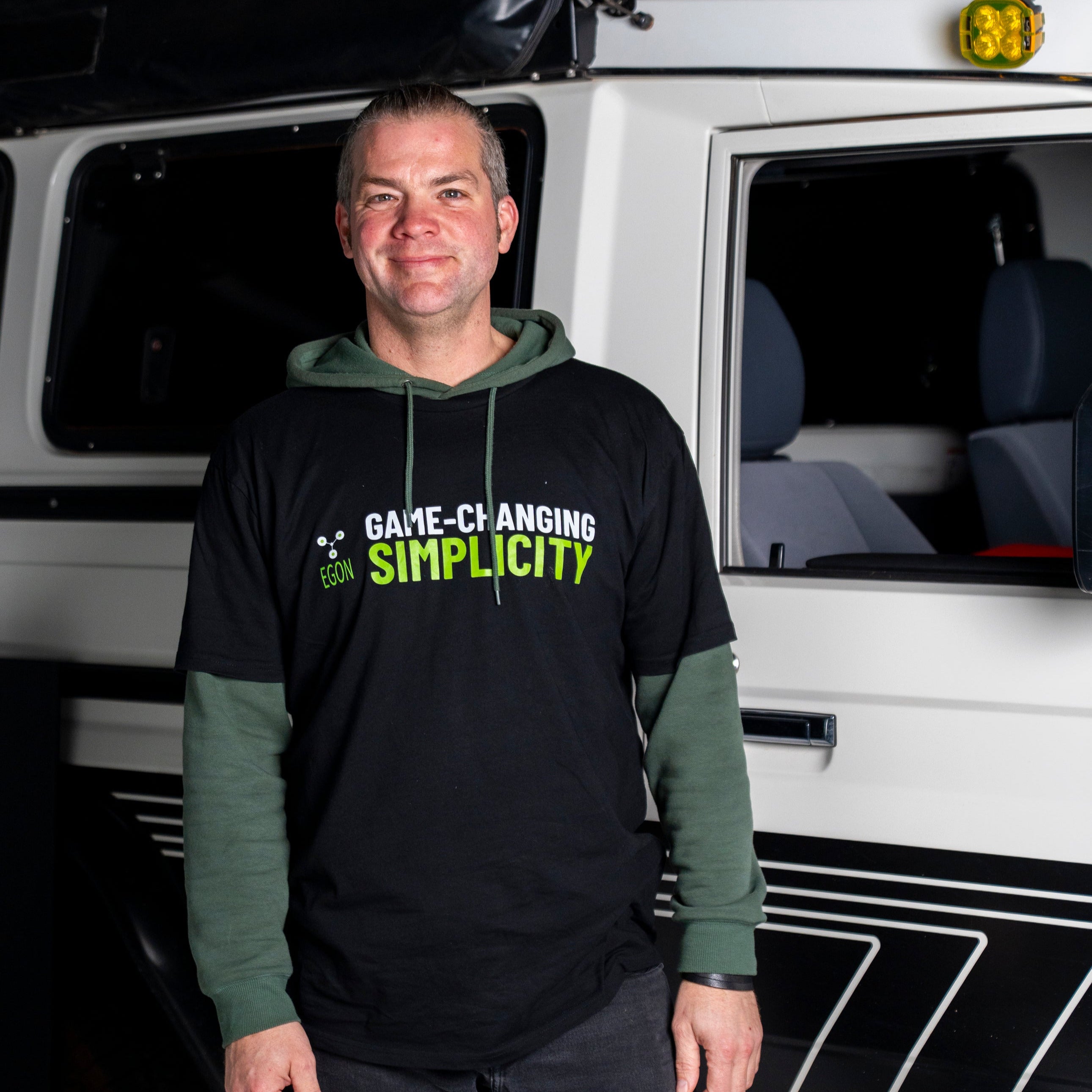 Man standing in front of a white van with text on his black hoodie.